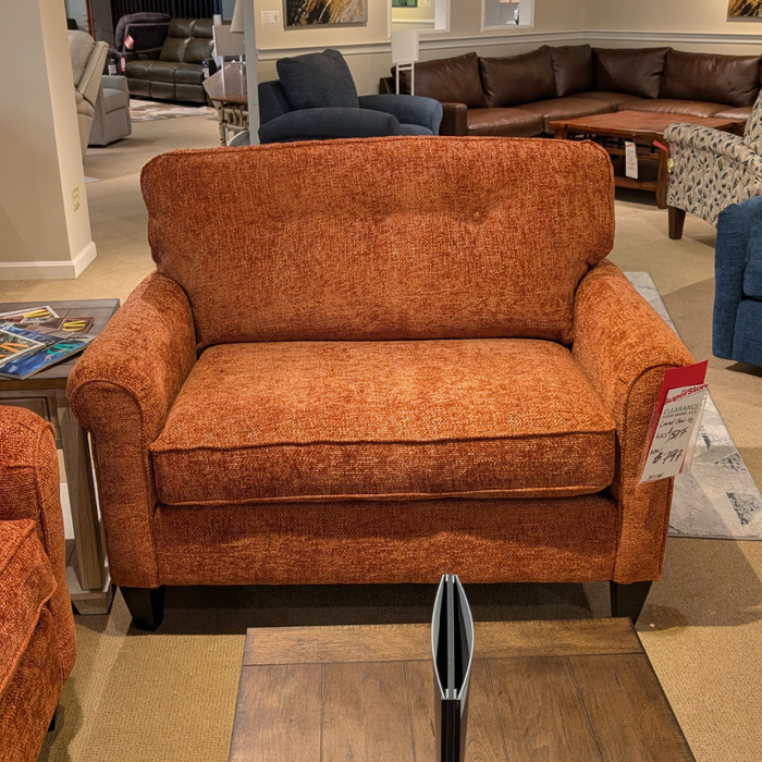 An orange-brown textured fabric loveseat in a furniture showroom, with a price tag attached to the right armrest.